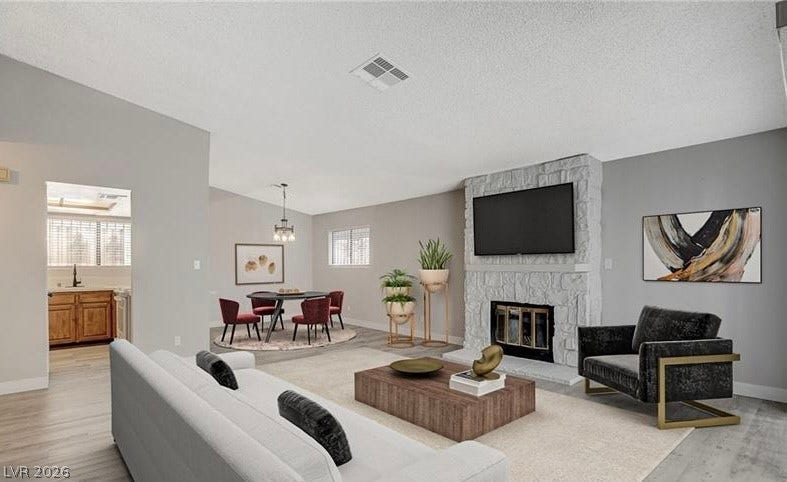 Living area with a stone fireplace, flowing into a dining space, and a peek into the kitchen.