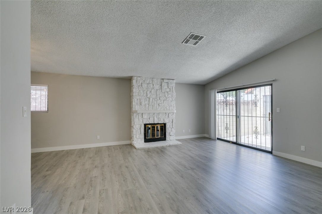 A whitewashed stone fireplace grounds this naturally illuminated living space with a vaulted ceiling.