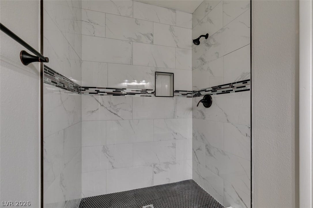 A well-appointed shower space features elegant marble-look tile walls and a contrasting mosaic floor.