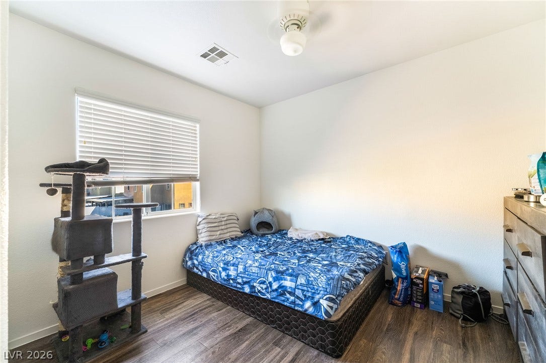 6275 Felicitas Avenue, Las Vegas, NV 89122 Rich wood-inspired floors and a wide window with blinds anchor this versatile bedroom space.