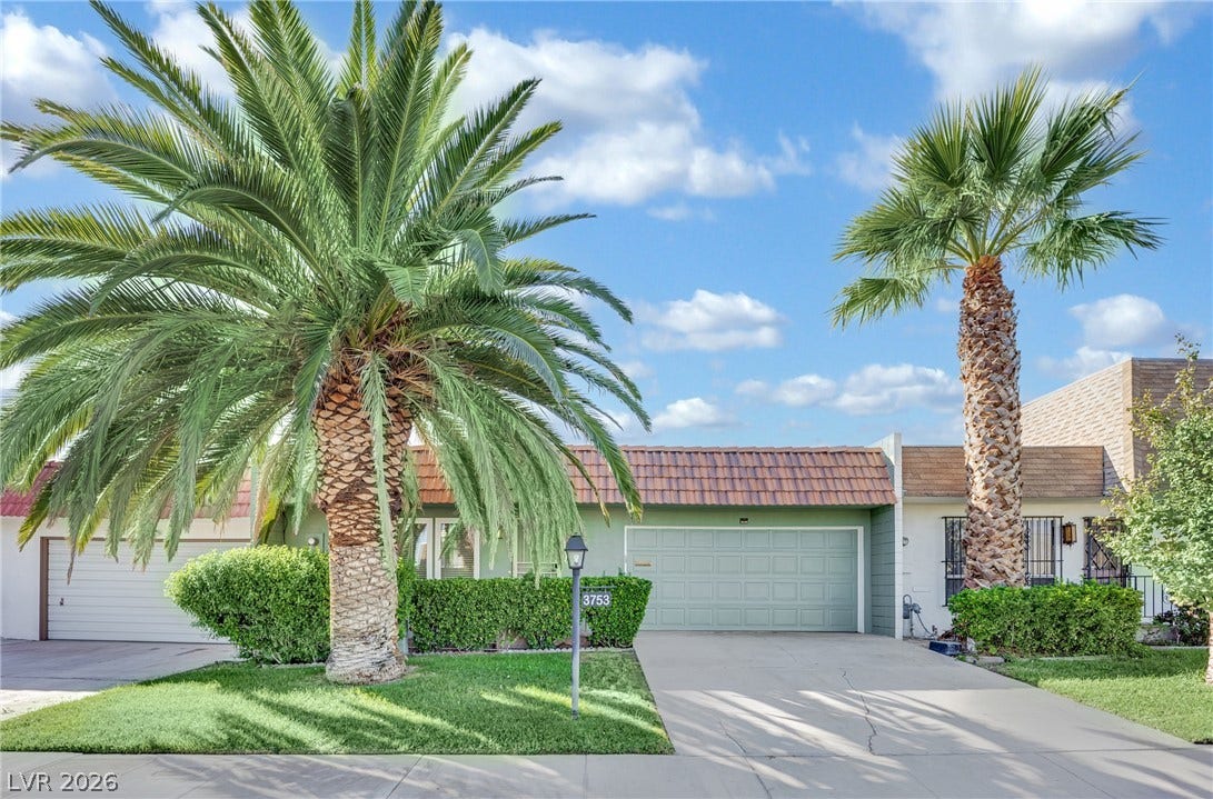 3753 Heritage Avenue, Las Vegas, NV 89121 Mature palm trees frame the concrete driveway leading to a two-car garage.