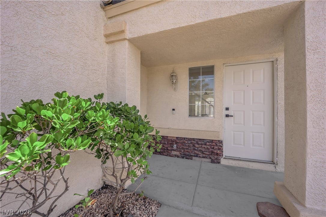 A welcoming covered entryway features textured stucco walls and a classic paneled front door.