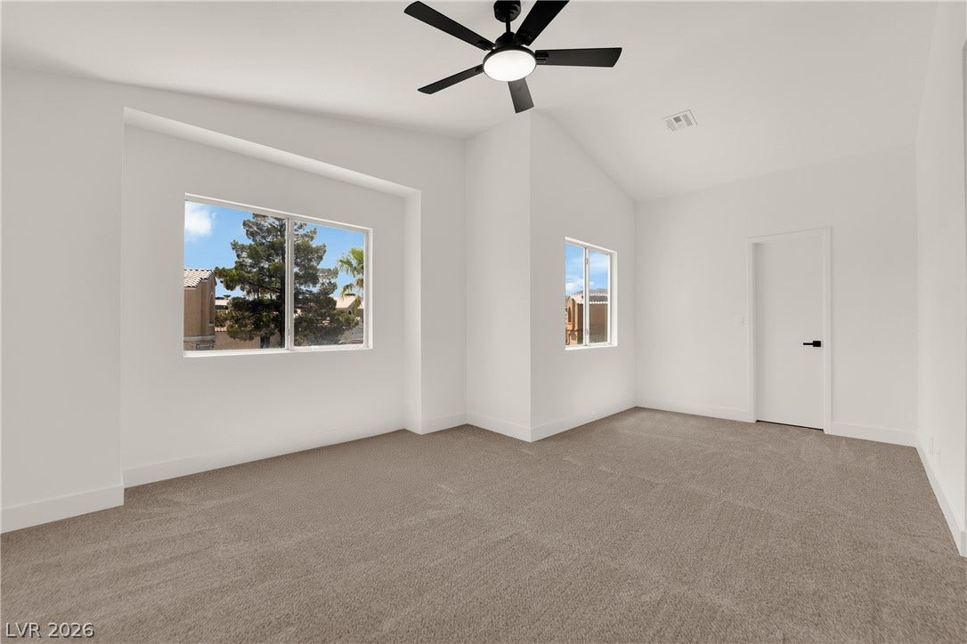 Vaulted ceilings and broad windows create an airy atmosphere in this carpeted bedroom.