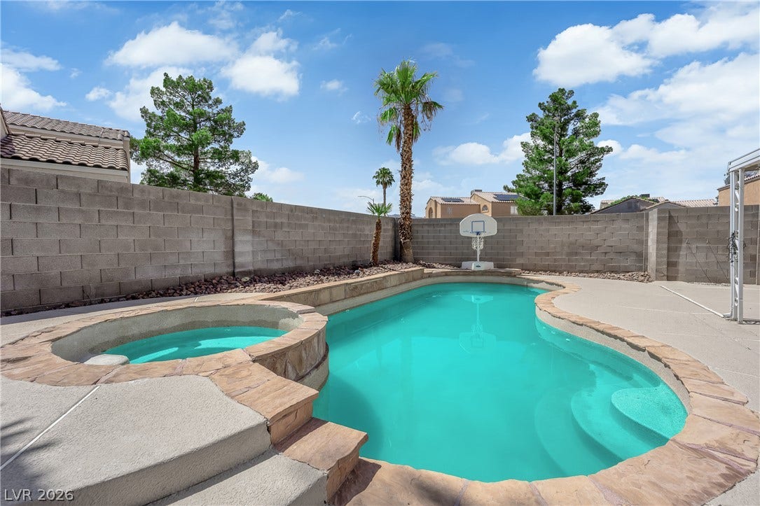 A sparkling in-ground pool and integrated spa sit surrounded by concrete decking and block fencing.