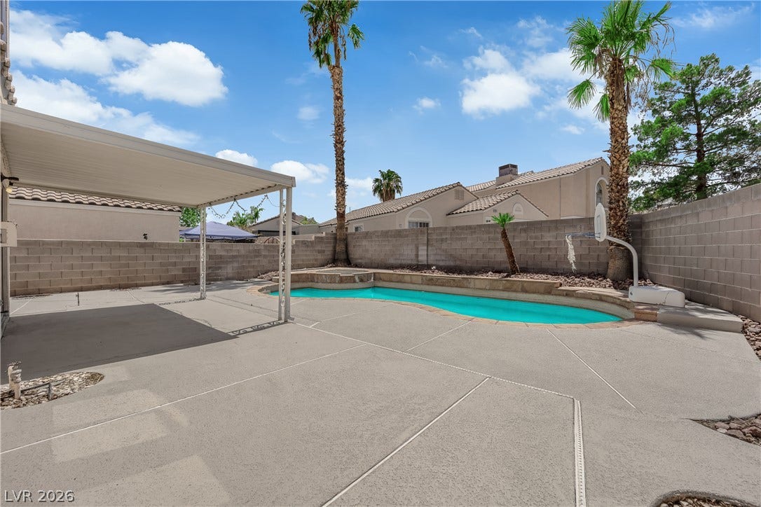 An inviting backyard oasis features a shimmering swimming pool alongside a covered concrete patio.