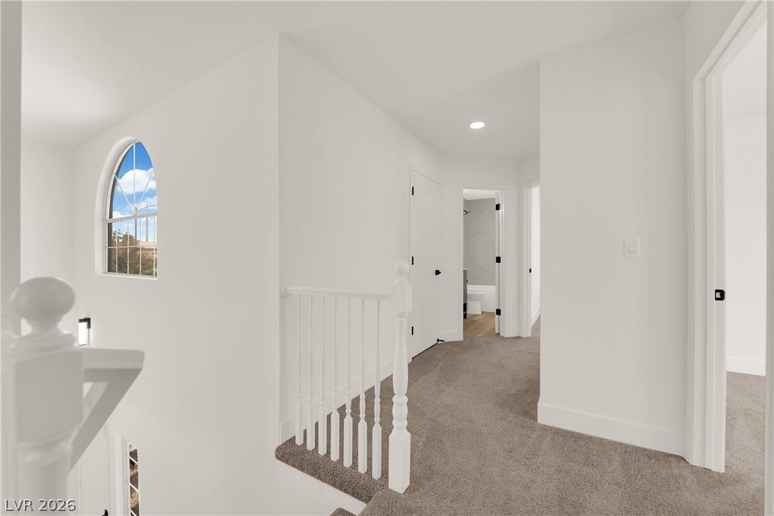 An arched window floods this carpeted upper hallway and open staircase with natural light.