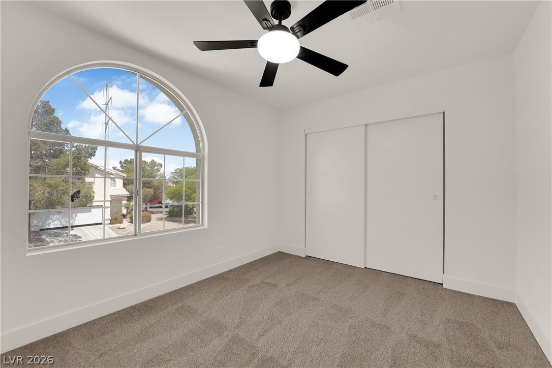 A classic arched window frames neighborhood views in this comfortable bedroom with soft carpeting.