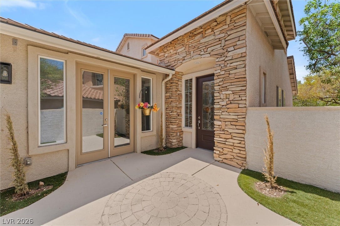 215 Sunset Shower Drive, Henderson, NV 89012 A welcoming stone-accented entryway features a patterned stone patio and glass-paneled doors.
