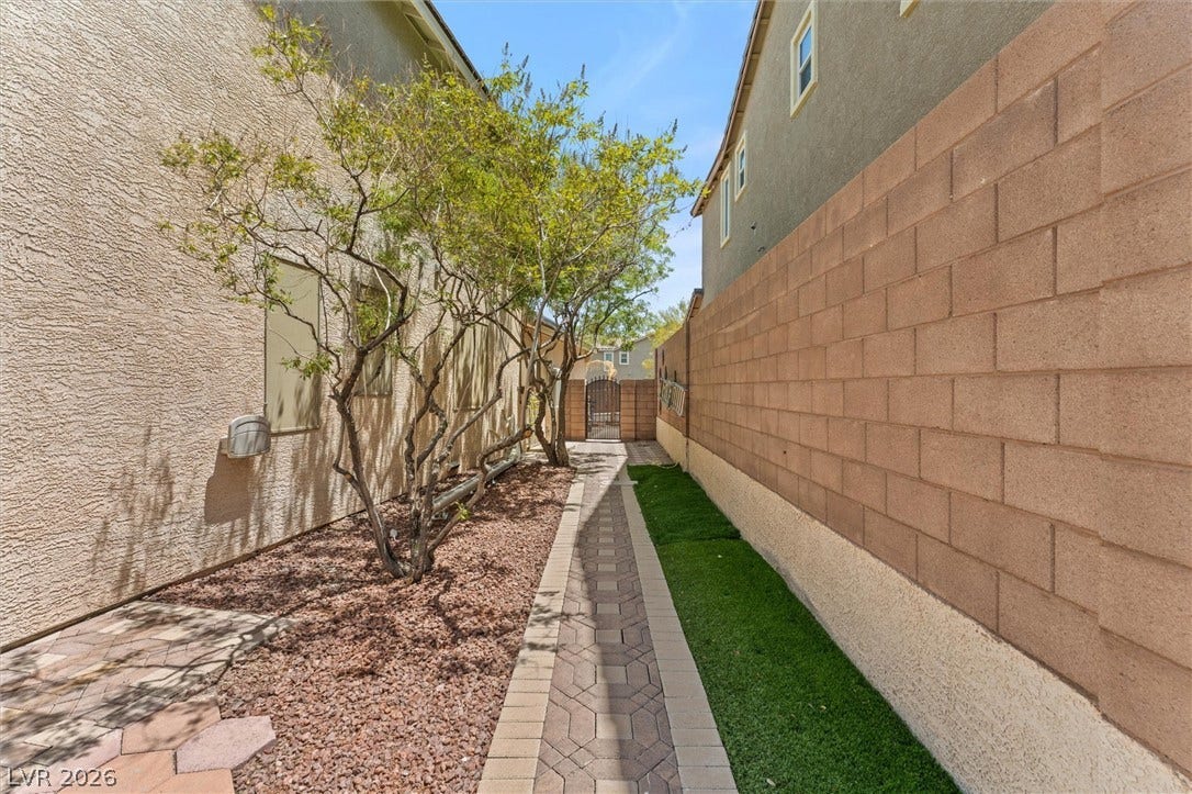 215 Sunset Shower Drive, Henderson, NV 89012 A paved walkway threads between a stucco exterior wall and a block fence.