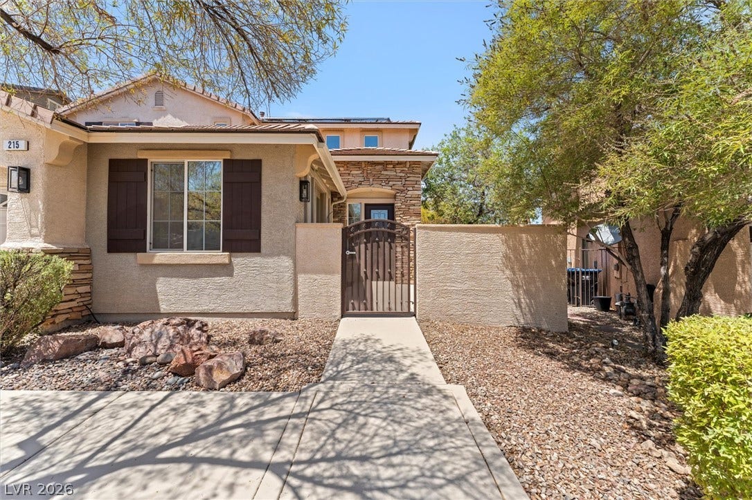 215 Sunset Shower Drive, Henderson, NV 89012 A gated entry path leads past stone accents and structured desert landscaping to the front door.
