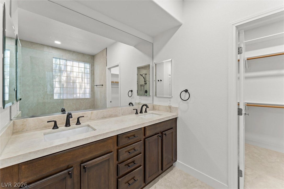 215 Sunset Shower Drive, Henderson, NV 89012 A spacious double vanity features stone countertops and adjacent walk-in closet access.
