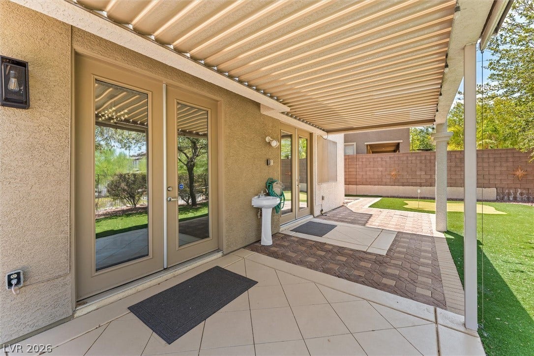 215 Sunset Shower Drive, Henderson, NV 89012 Double glass doors open directly to a covered patio flanked by pavers and a lawn.