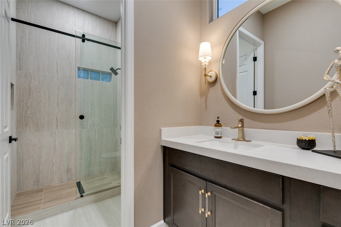 2532 Faiss Drive, Las Vegas, NV 89134 An elegant vanity with stone counters stands adjacent to a modern glass-enclosed walk-in shower.