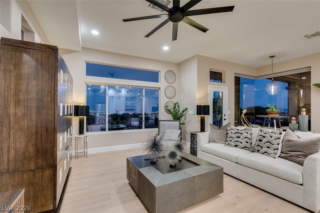 2532 Faiss Drive, Las Vegas, NV 89134 A spacious living room features light hardwood flooring and oversized windows framing evening views.