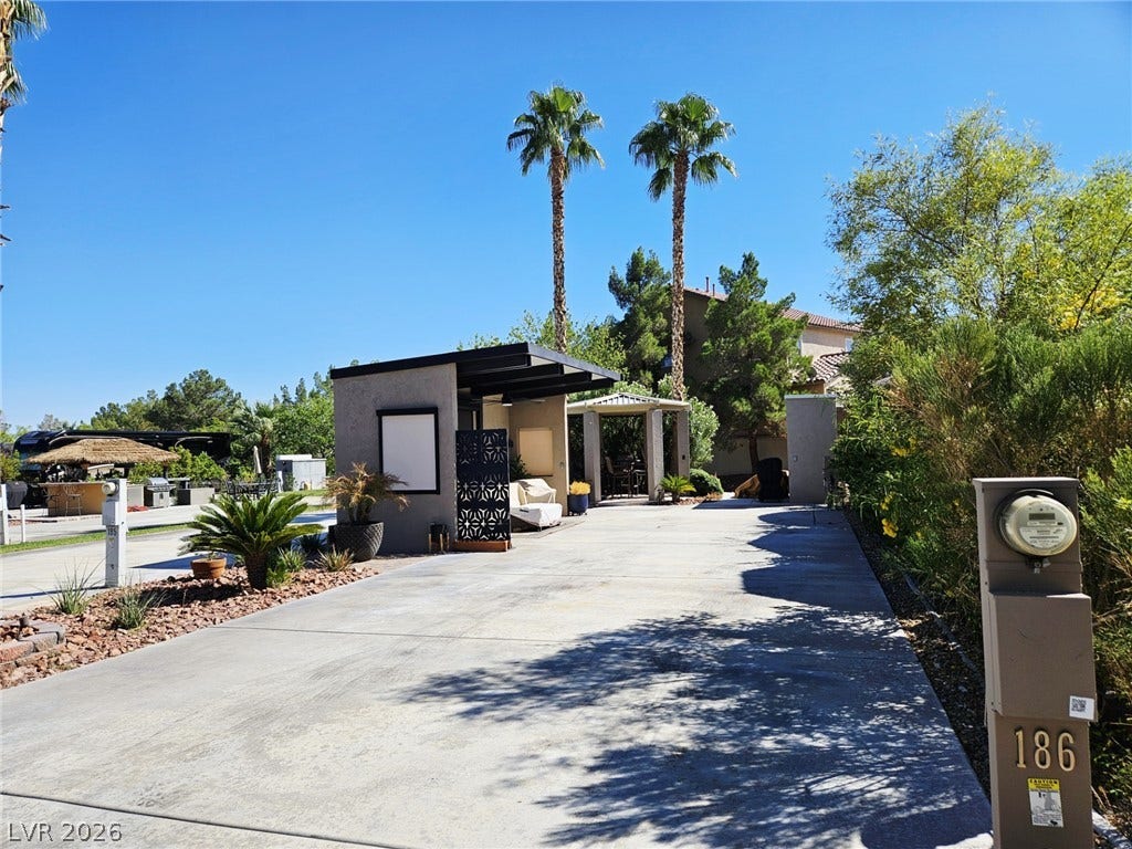 8175 Arville Street, #186, Las Vegas, NV 89139 An expansive concrete driveway leads past a modern privacy structure framed by soaring palm trees.