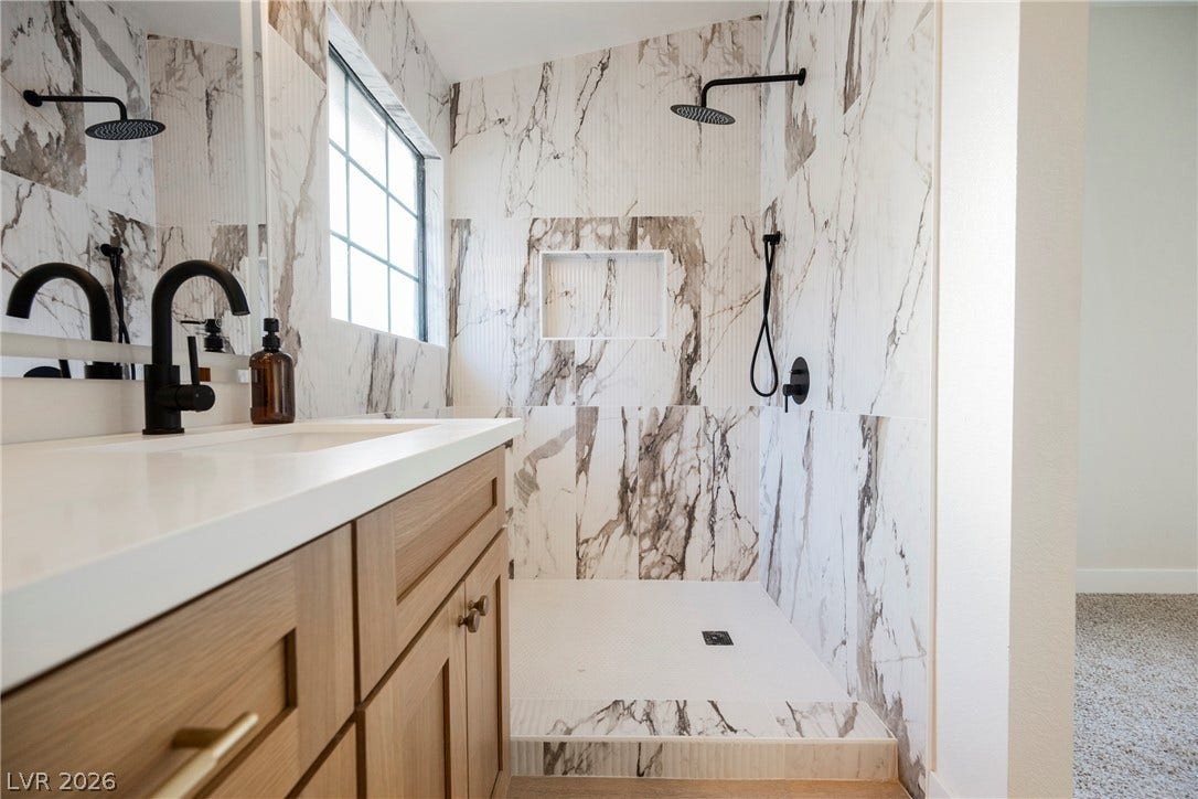 4877 Fiesta Lakes Street, Las Vegas, NV 89130 Floor-to-ceiling stone tile surrounds the curbless walk-in shower alongside a modern vanity.