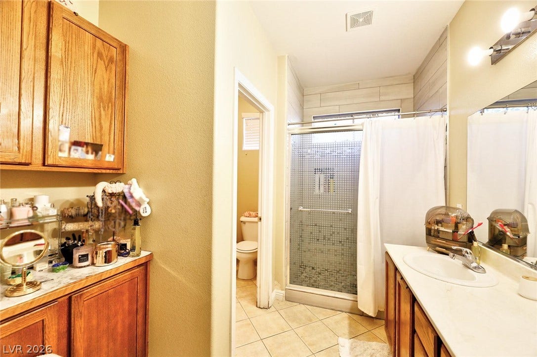 Tiled flooring pairs with wooden cabinetry and a built-in shower in this functional bathroom layout.