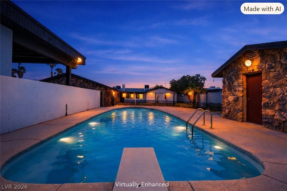 A sparkling in-ground pool is framed by concrete decking and stone-accented outbuildings.