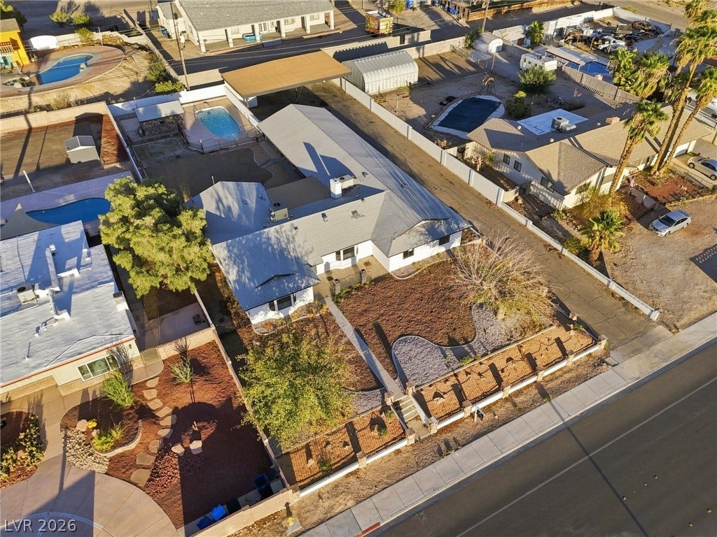 Aerial view reveals a low-profile residential home with shingle roofing and an in-ground pool.