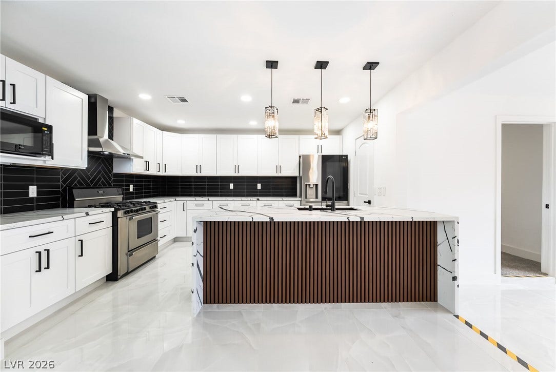 Striking dark backsplash and custom cabinetry flank a generous kitchen island under high ceilings.