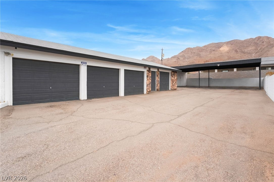 An expansive asphalt driveway leads to multiple garage bays set against a dramatic mountain backdrop.