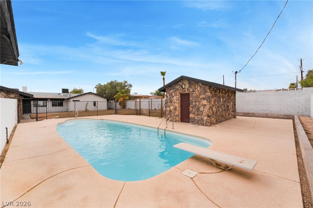 An inviting backyard pool area features a spacious concrete deck and a stone outbuilding.