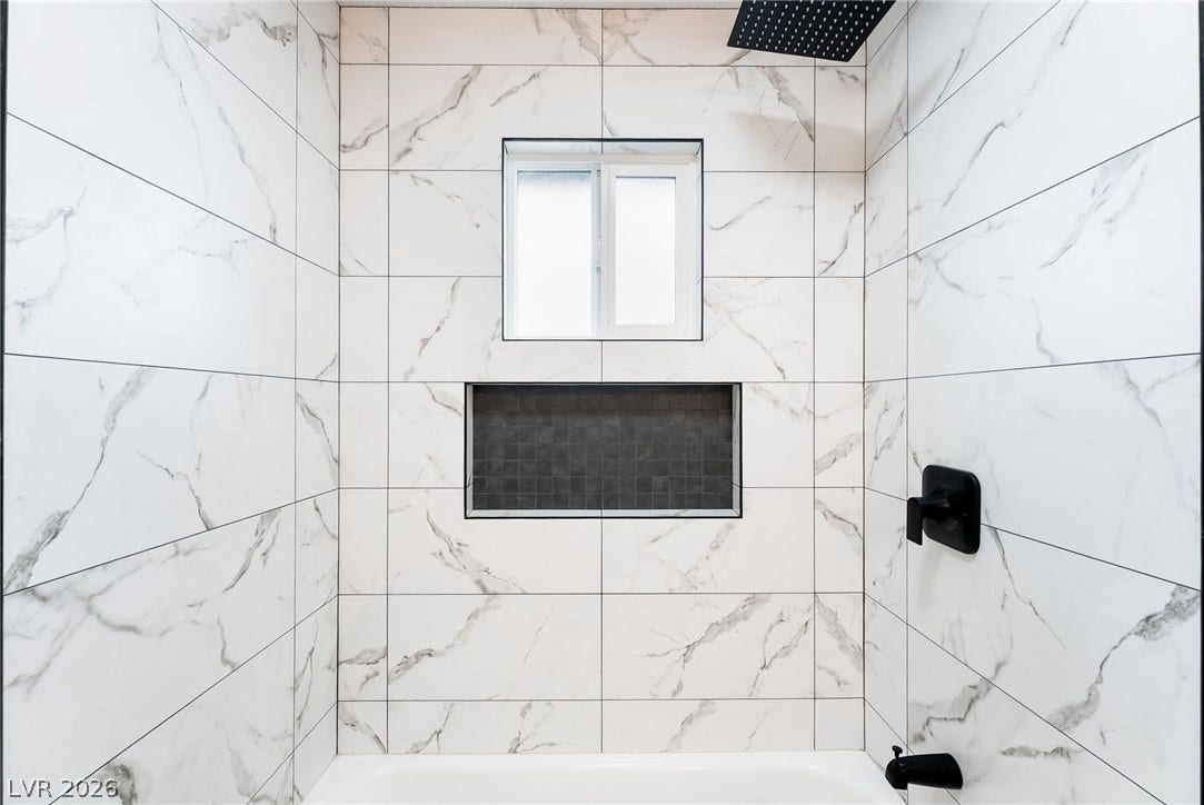 Elegant marble-patterned tile surrounds a modern shower alcove with sleek dark hardware and built-in shelving.