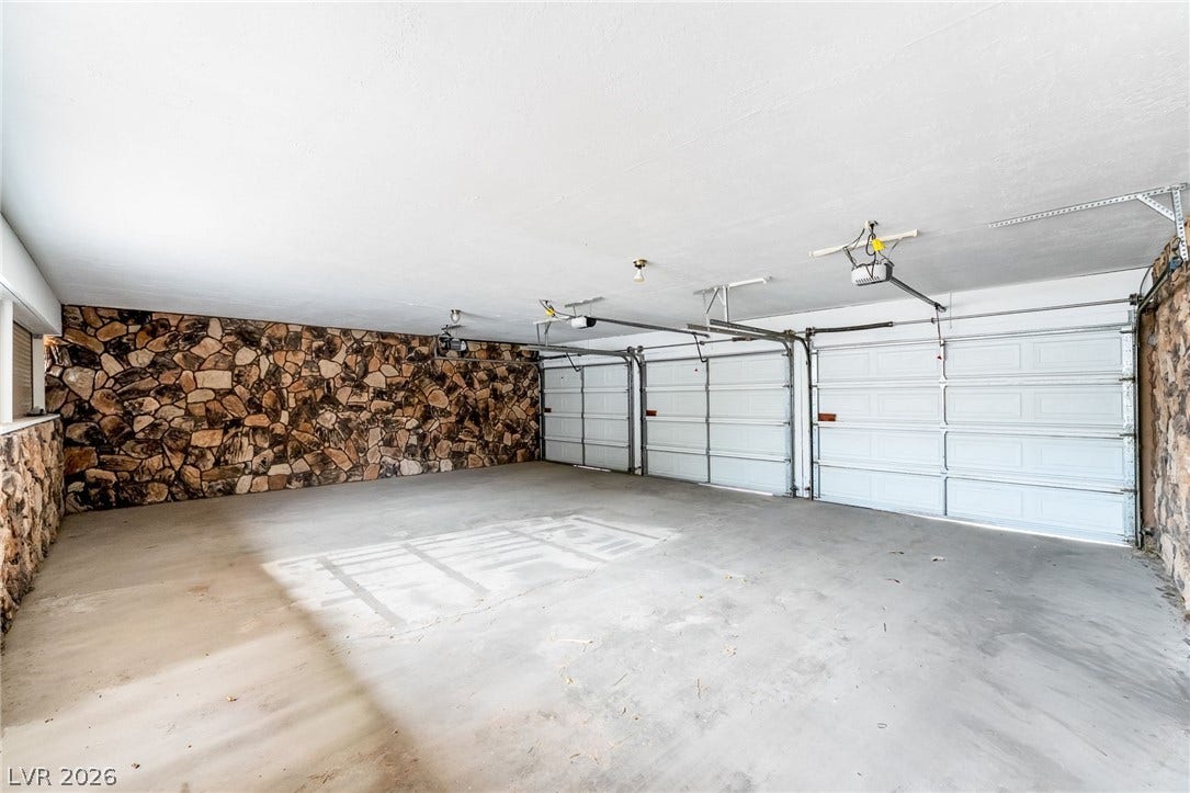 A spacious three-car garage displays distinctive stone accent walls and a solid concrete floor.