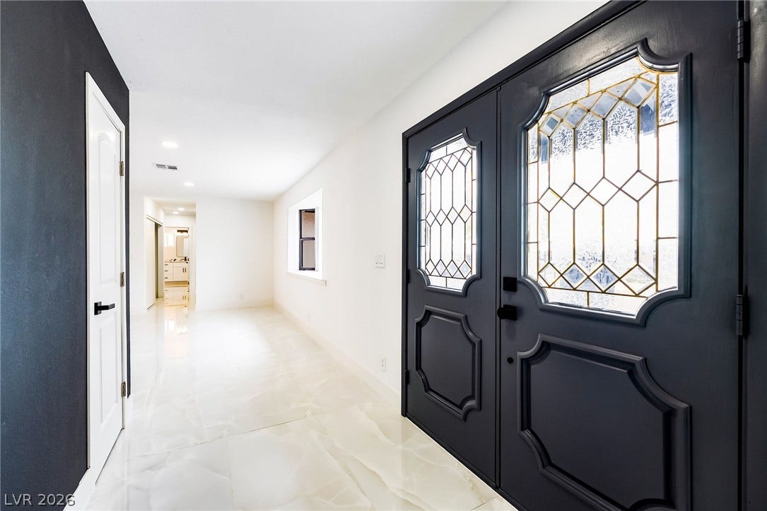 Ornate double doors with decorative glass panels welcome guests into a light-filled entry corridor.