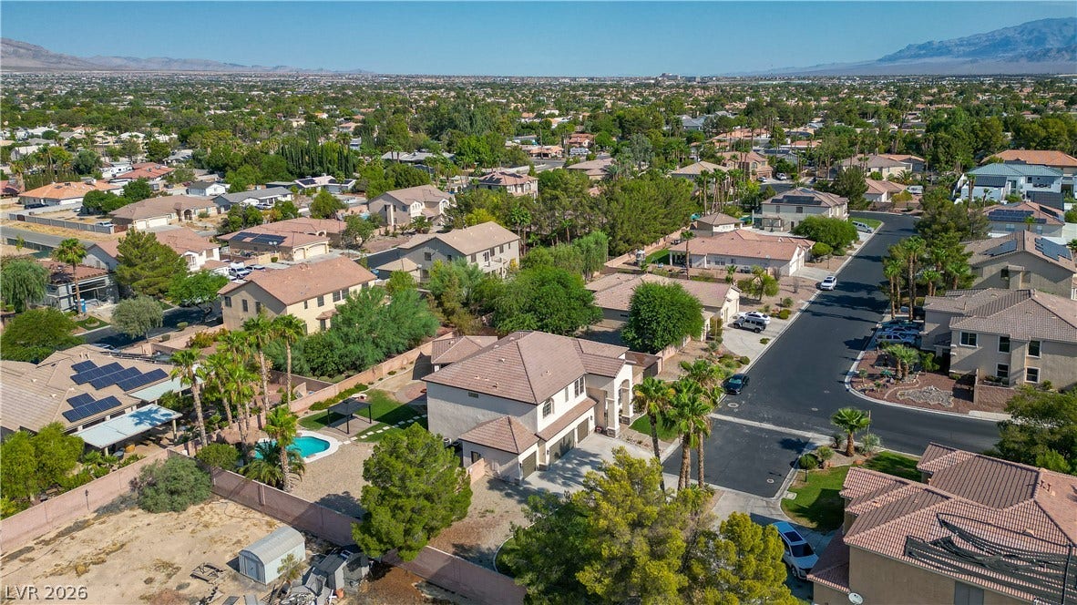 A quiet residential street winds through an established neighborhood backed by distant mountains.