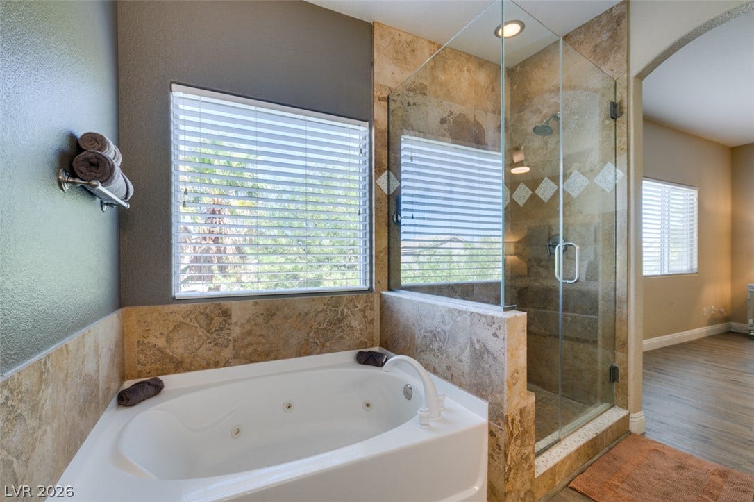 3166 E Eldorado Lane, Las Vegas, NV 89120 Natural stone tile surrounds a built-in soaking tub next to a glass-enclosed shower.