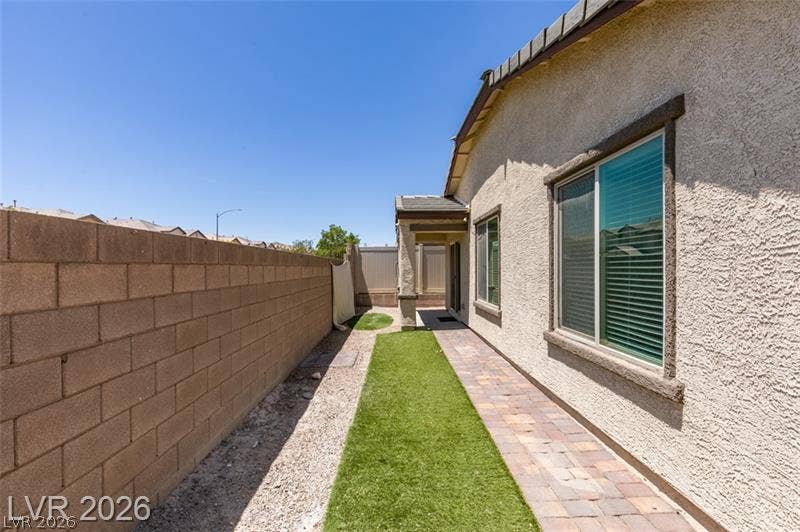 A paved walkway and tidy turf run alongside the textured stucco exterior wall.