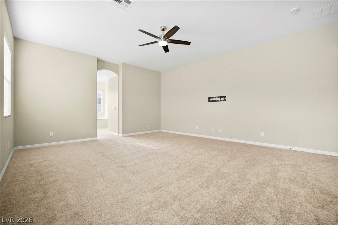 7230 Fresh Harvest Avenue, Las Vegas, NV 89131 A spacious, naturally illuminated room boasts soft carpeting and a contemporary ceiling fan, offering a comfortable atmosphere.