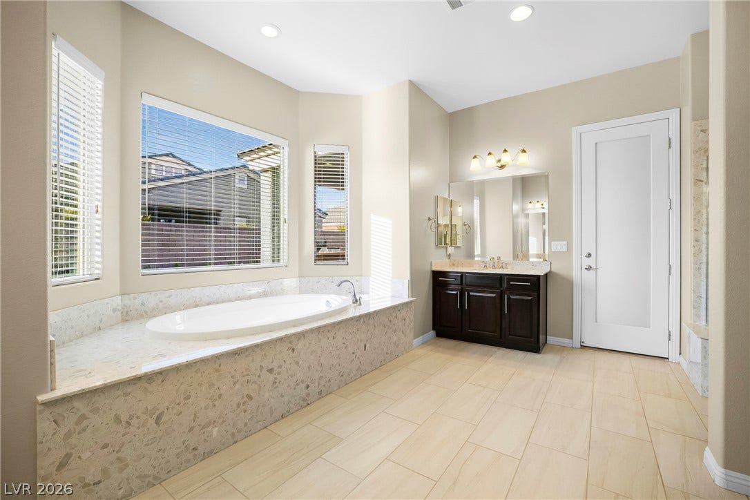 7230 Fresh Harvest Avenue, Las Vegas, NV 89131 Indulge in a tranquil retreat featuring a spacious soaking tub beneath sun-lit windows, paired with a stylish vanity and generous counter space.