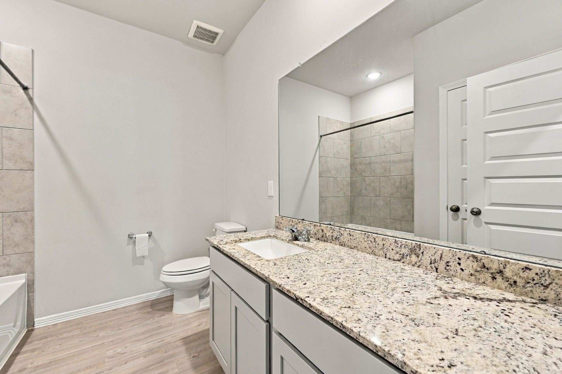 5702 Fresh View Court, Katy, TX 77493 The spacious secondary bathroom showcases a beautifully coordinated combination of granite countertops, shaker-style cabinetry, & an expansive vanity offering generous counter space. A large wall mirror enhances the room's open feel, while wood-look flooring, recessed lighting, & a neutral color palette complete the inviting design.