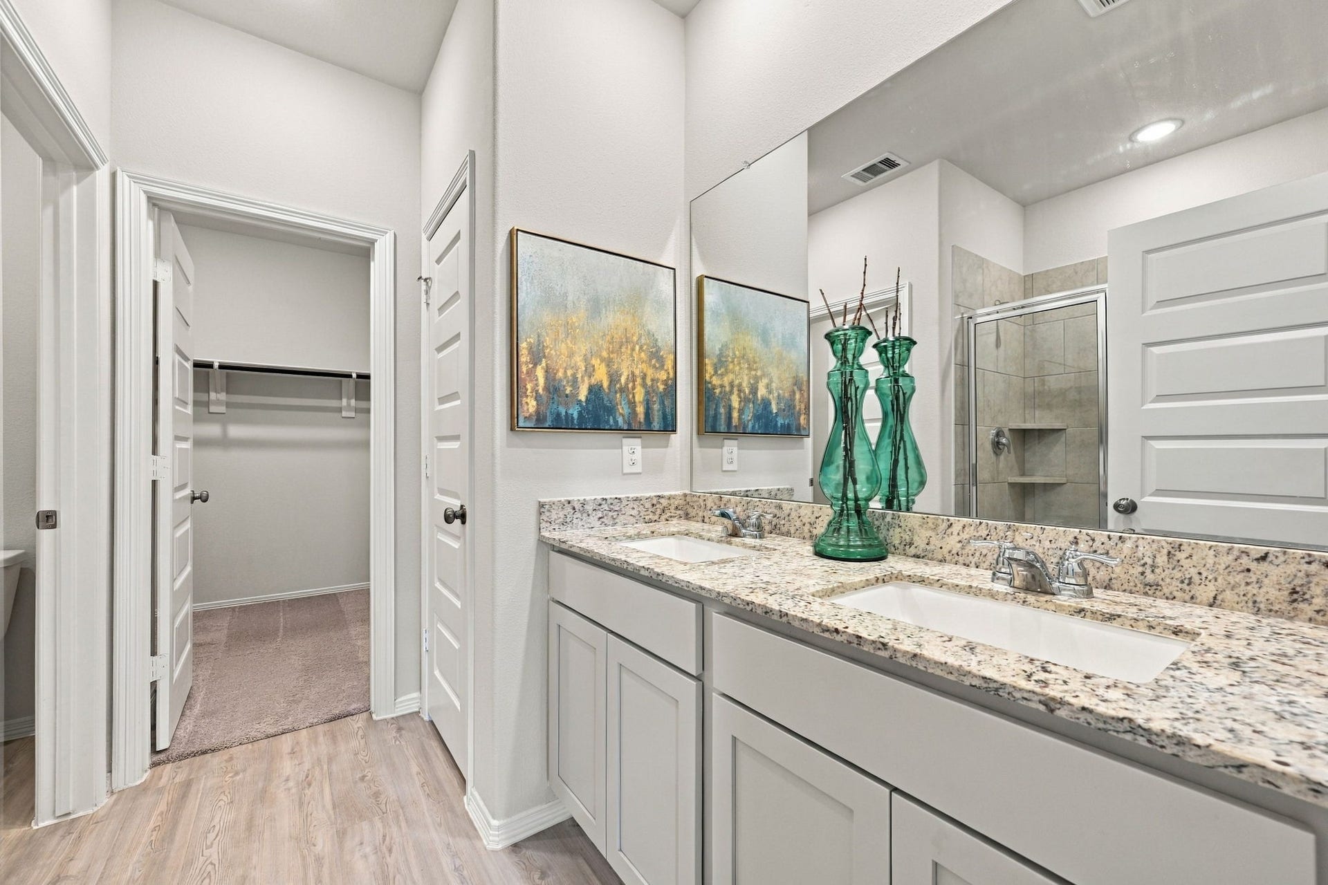 5702 Fresh View Court, Katy, TX 77493 The beautifully finished primary bathroom showcases an expansive dual-sink vanity topped with granite countertops, complemented by elegant shaker-style cabinetry & an oversized wall mirror. Recessed lighting, generous counter space, & ample storage add to the room's functionality, while the nearby walk-in closet provides exceptional convenience.