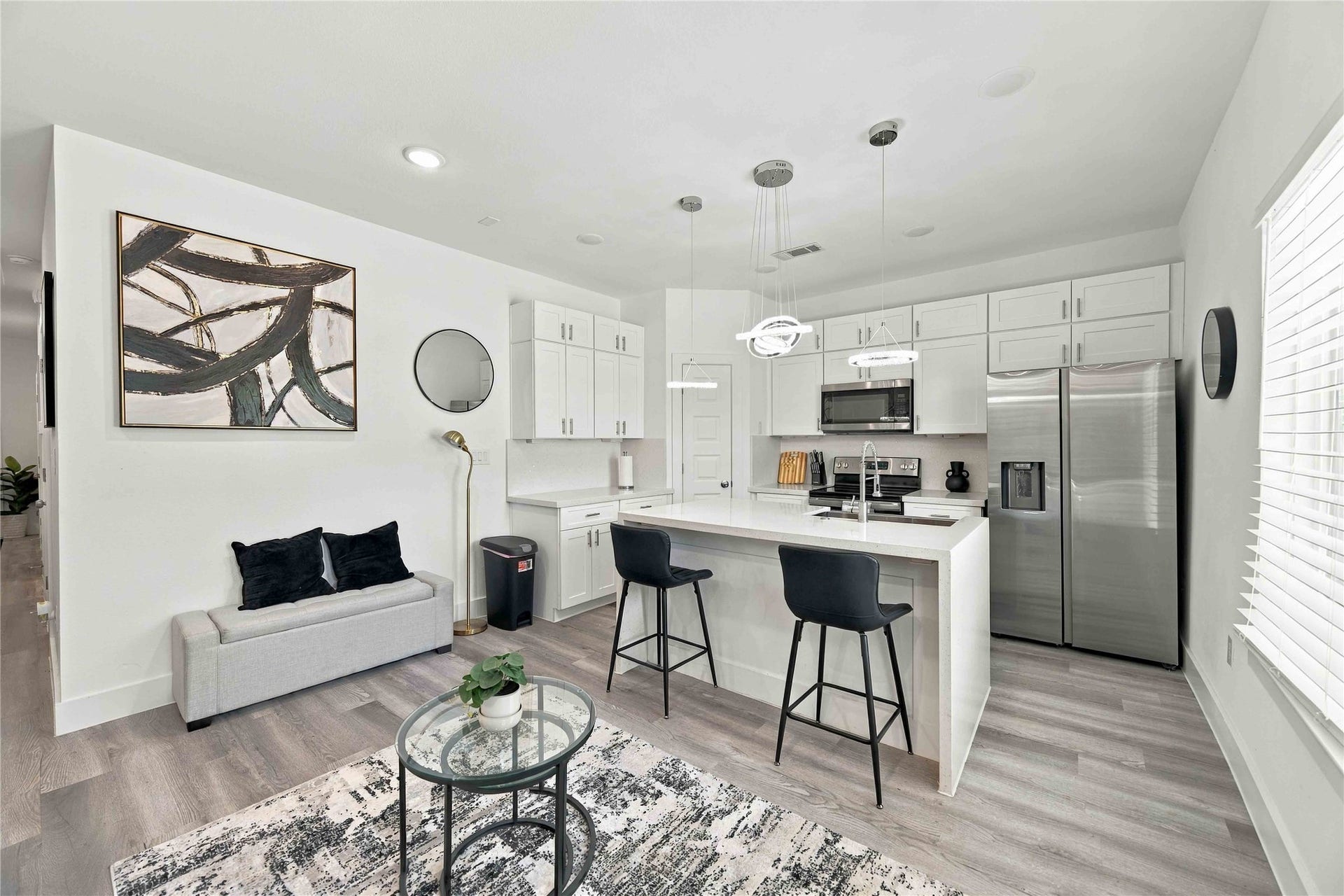 This sleek kitchen understood the assignmentwaterfall quartz island, stainless-steel appliances, crisp cabinetry, and statement lighting.