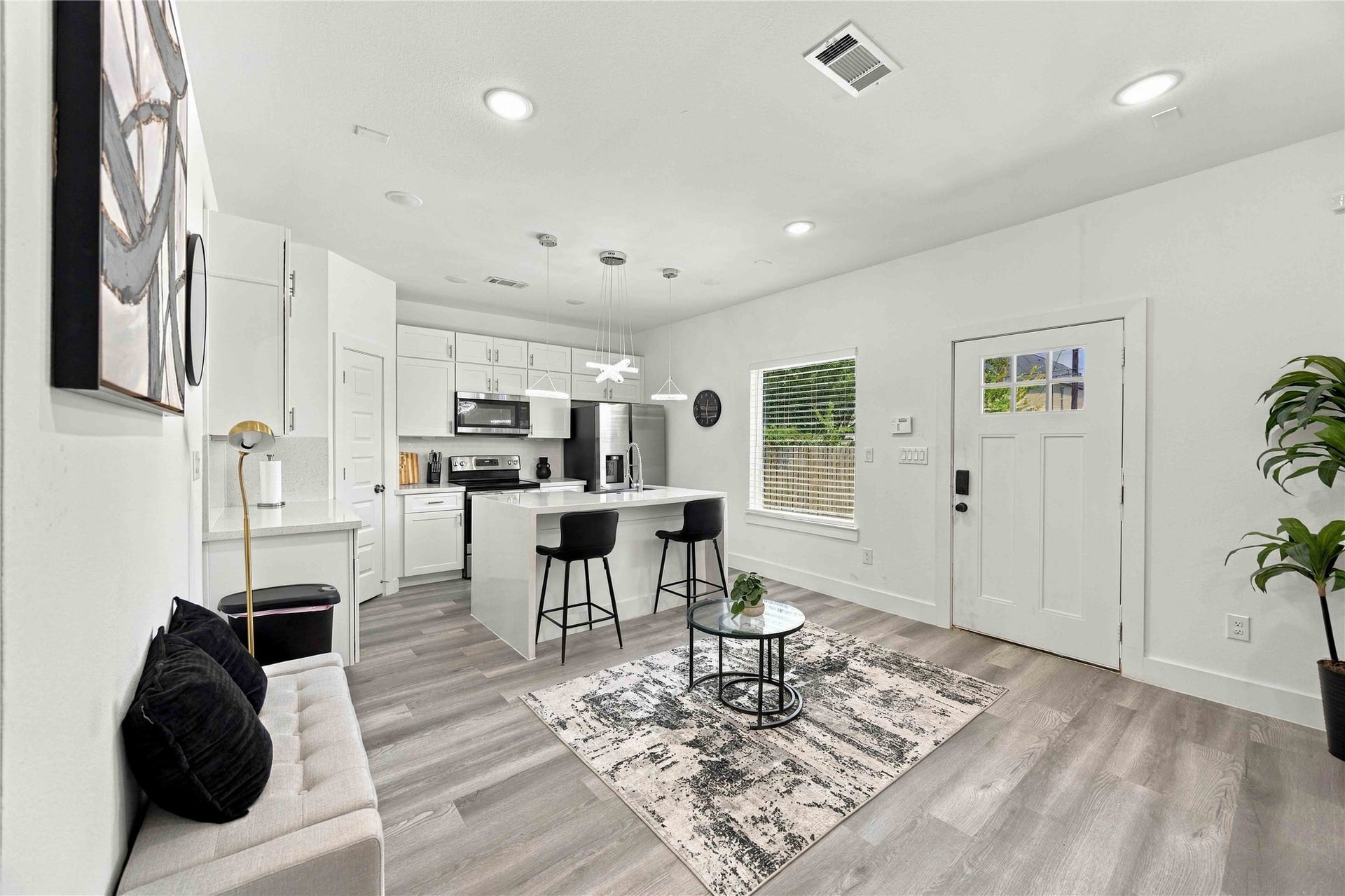 Open-concept living and kitchen area featuring modern finishes, quartz countertops, stainless steel appliances, and stylish pendant lighting.