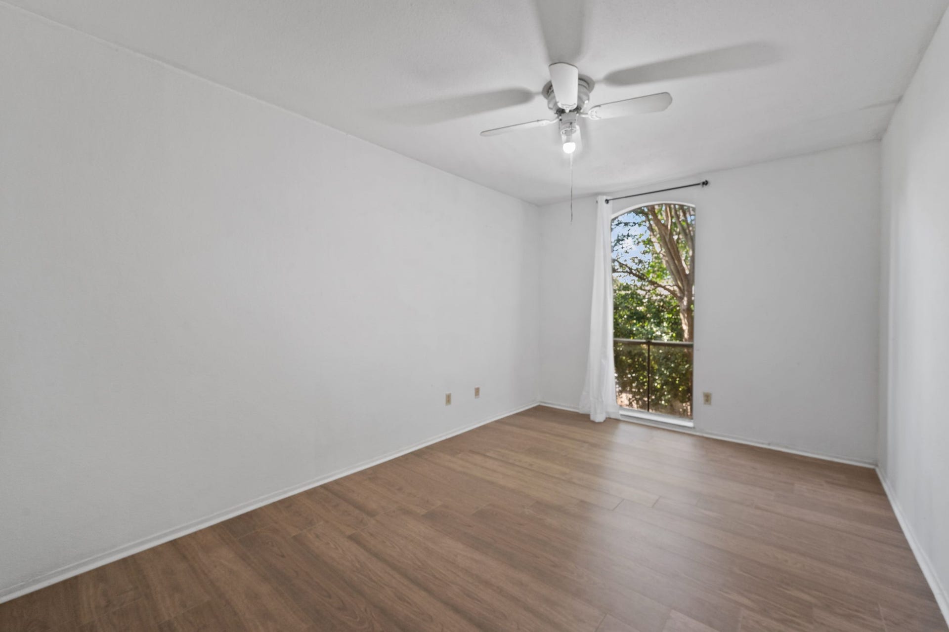 4649 Wild Indigo Street, #337, Houston, TX 77027 Bright and airy room featuring elegant wood flooring, a ceiling fan, and a large arched window offering serene views of lush greenery.