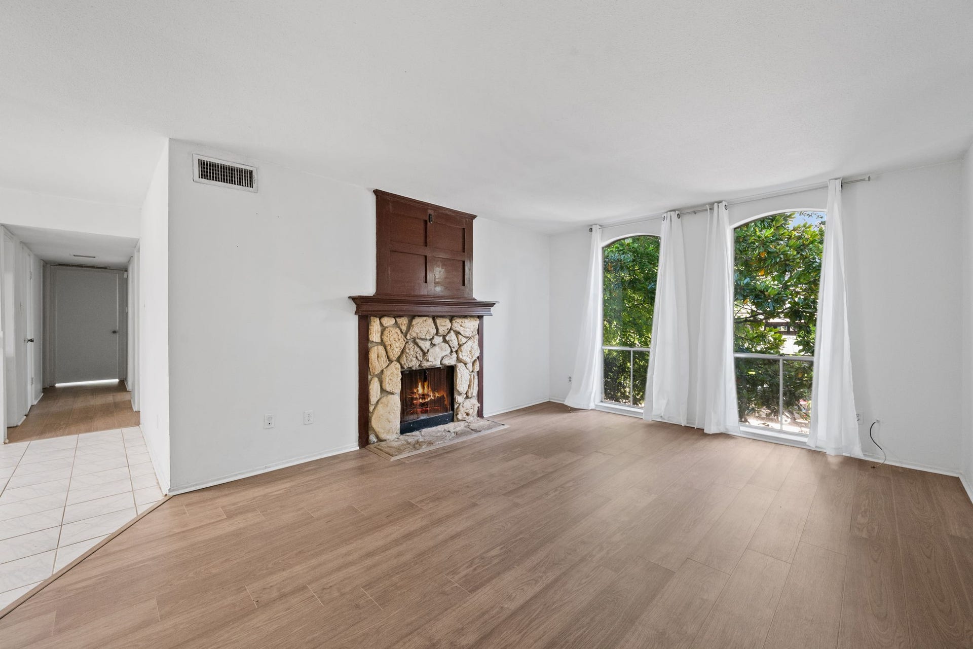 4649 Wild Indigo Street, #337, Houston, TX 77027 Bright living room featuring large windows with serene views, a cozy stone fireplace, and elegant wood flooring.