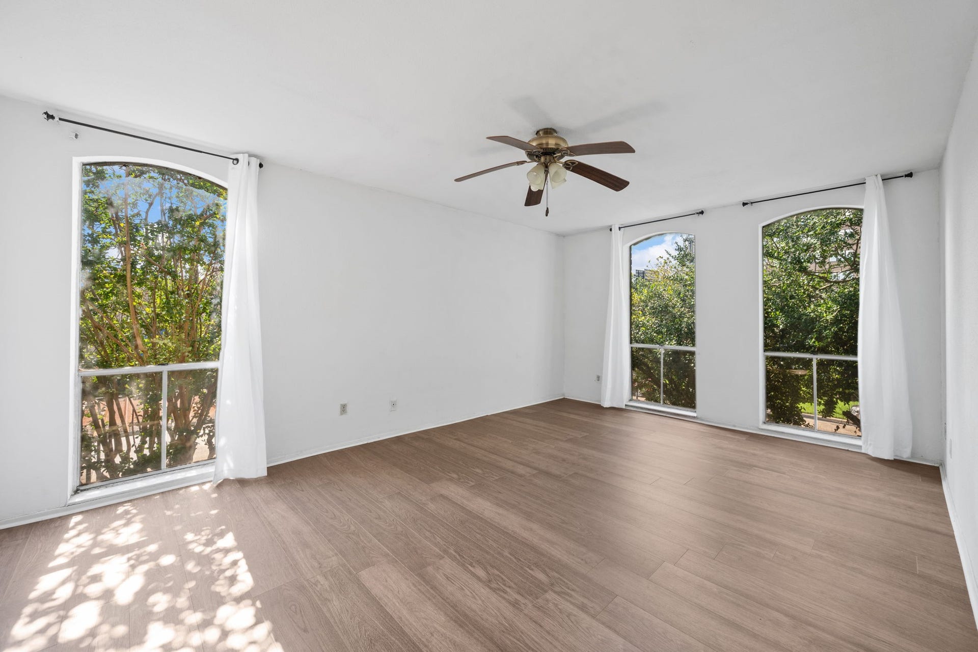 4649 Wild Indigo Street, #337, Houston, TX 77027 Bright and spacious room featuring elegant wood flooring, large arched windows with lush green views, and a stylish ceiling fan.
