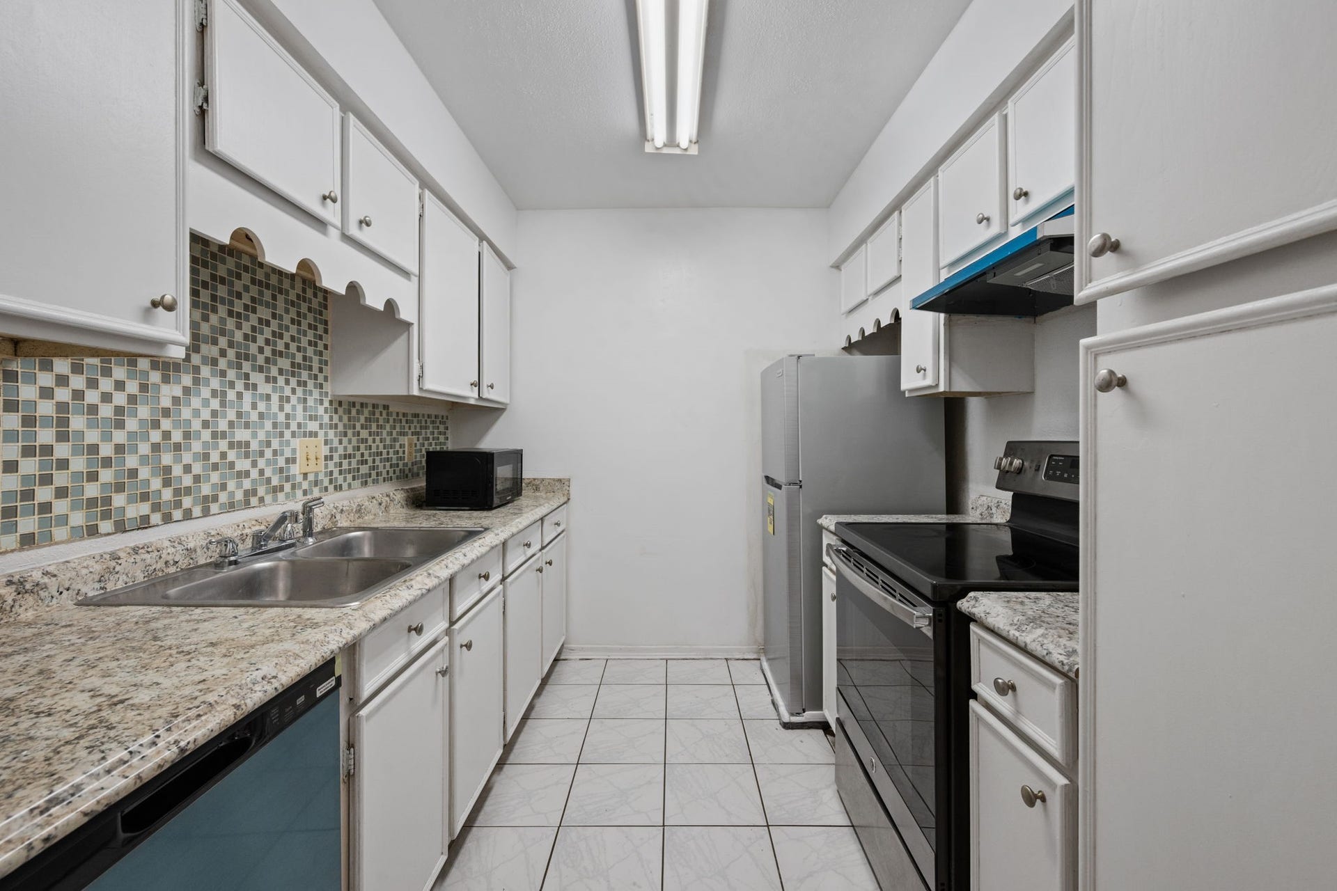 4649 Wild Indigo Street, #337, Houston, TX 77027 Charming kitchen with sleek granite countertops, modern appliances, and a stylish mosaic tile backsplash, offering ample storage space in crisp white cabinetry.