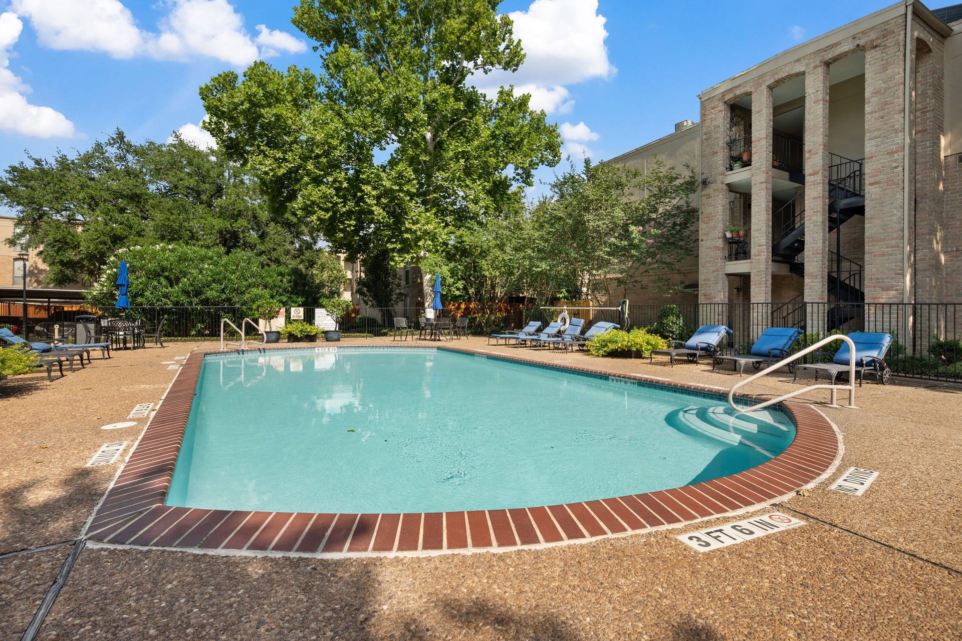 4649 Wild Indigo Street, #337, Houston, TX 77027 Relax by the sparkling pool surrounded by lush greenery and comfortable lounge chairs, offering a serene outdoor retreat.