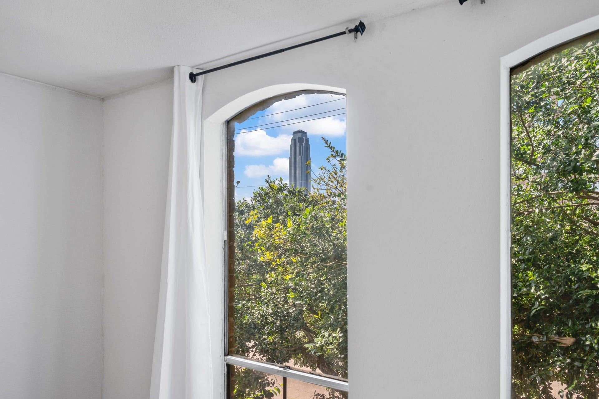 4649 Wild Indigo Street, #337, Houston, TX 77027 Bright, airy interior with a charming arched window offering views of lush greenery and a cityscape beyond.