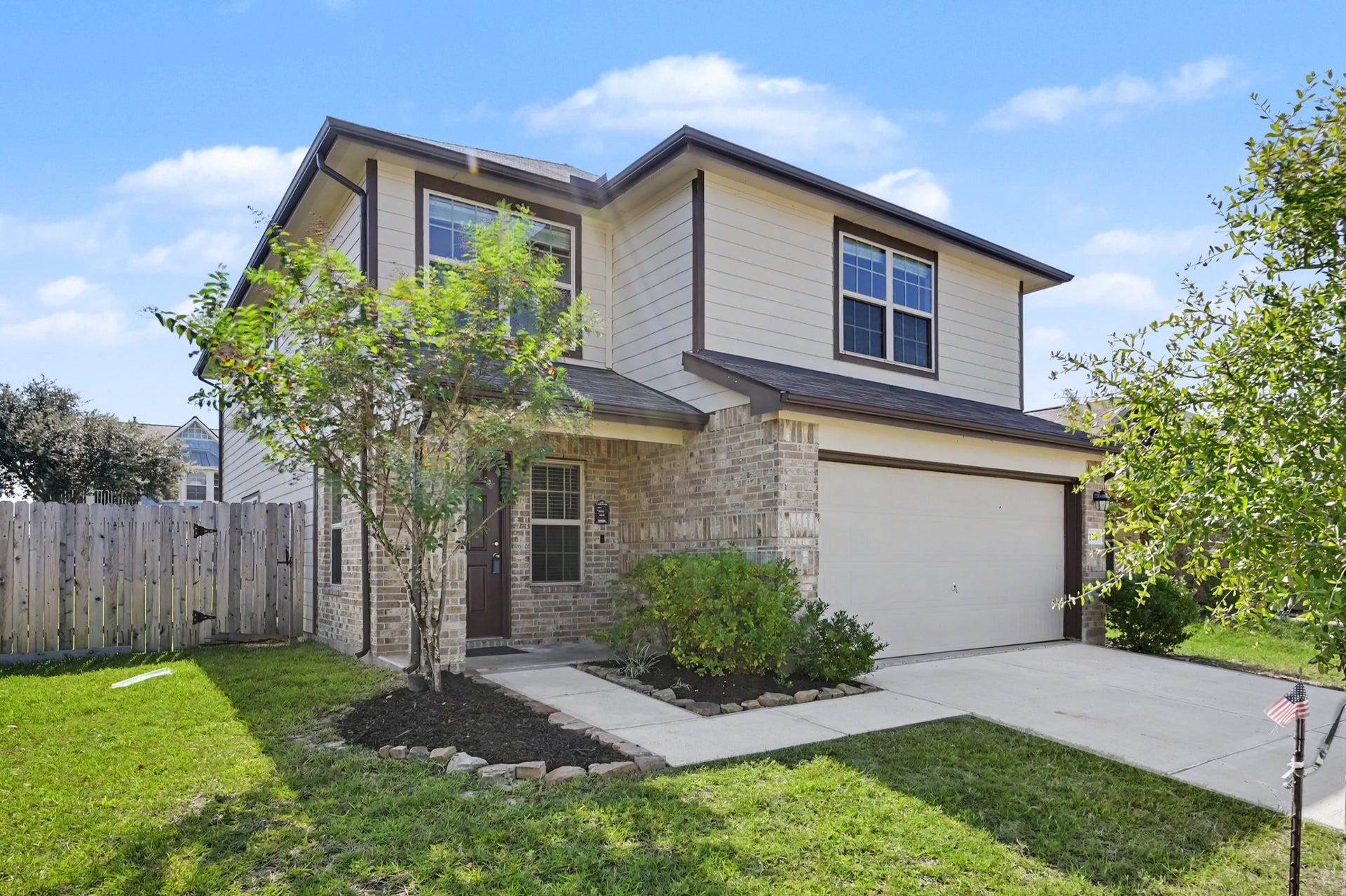 Beautiful two-story home featuring attractive brick and siding exterior, mature trees, landscaped flower beds, a welcoming covered front entry and double wide driveway.