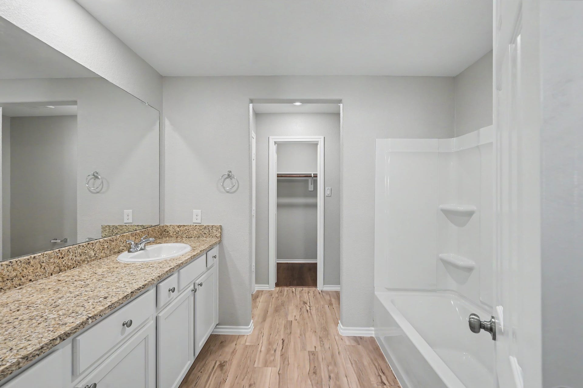 Spacious primary bath featuring an extended granite vanity, white cabinetry, tub/shower combination, and access to a walk-in closet.