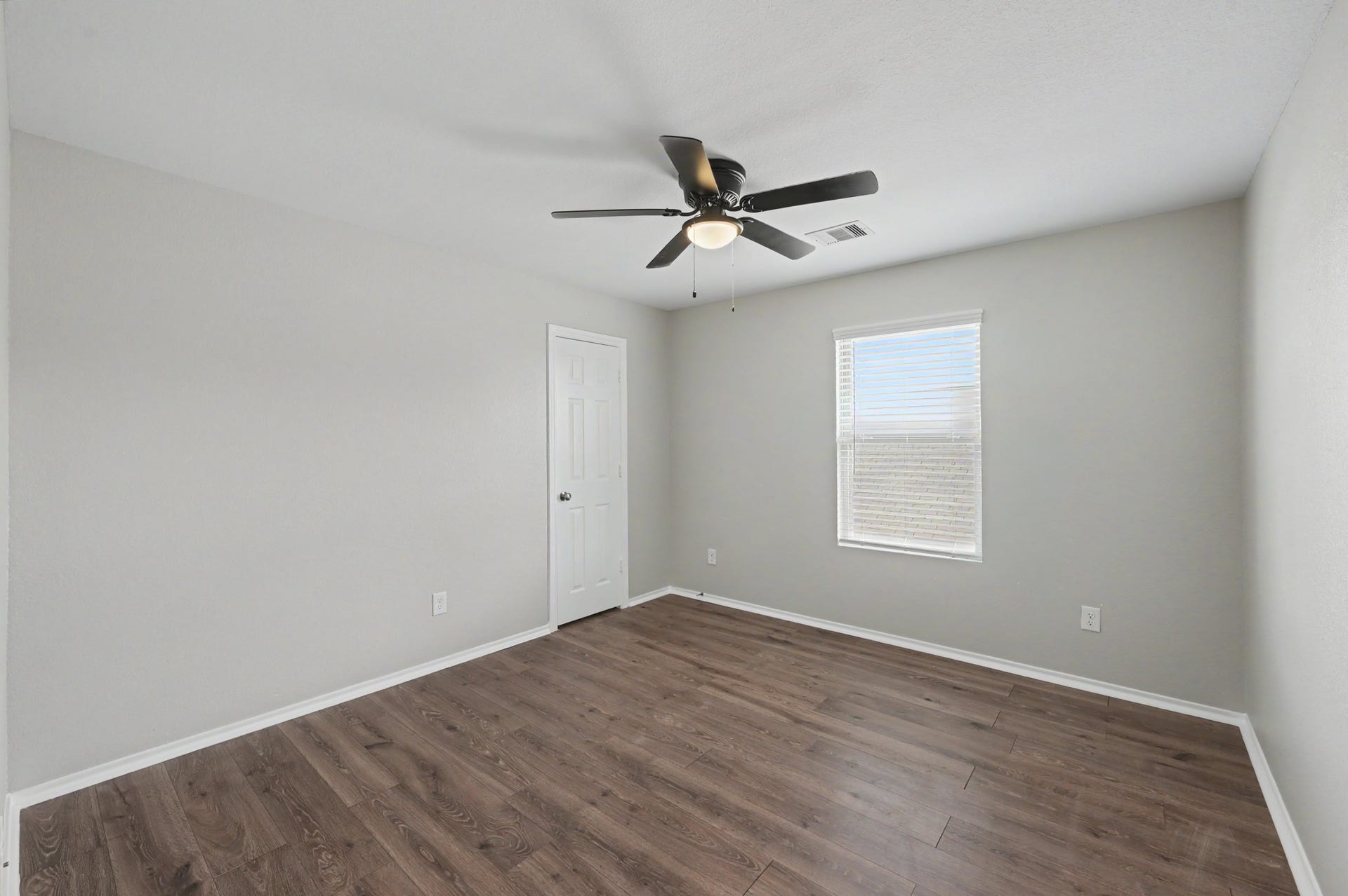 Spacious secondary bedroom featuring wood-look flooring, neutral paint tones, ceiling fan, and a large window providing natural light.