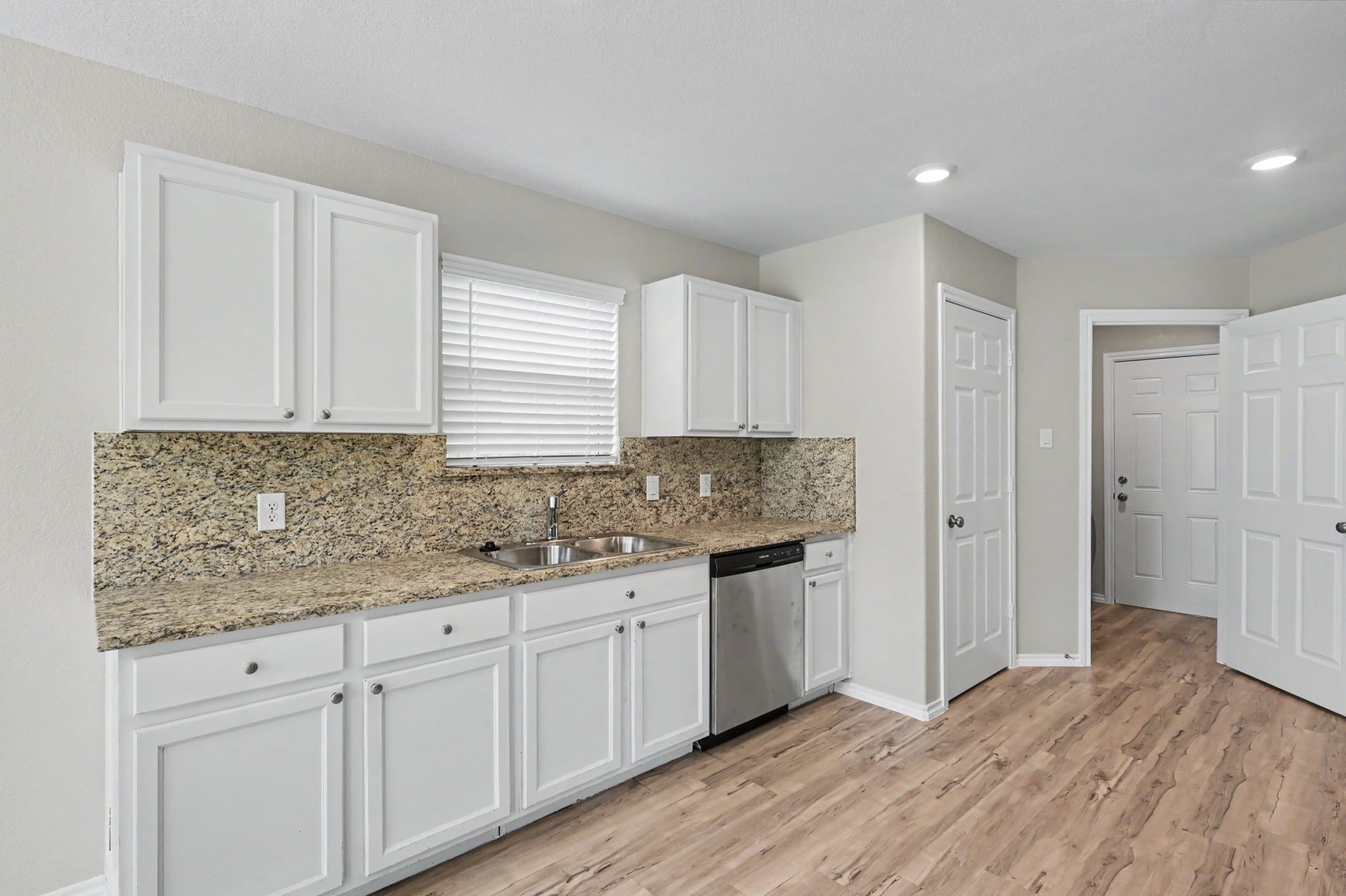 Additional kitchen view showcasing countertops with matching backsplash, white cabinetry, double sink, stainless steel dishwasher, and generous counter space.