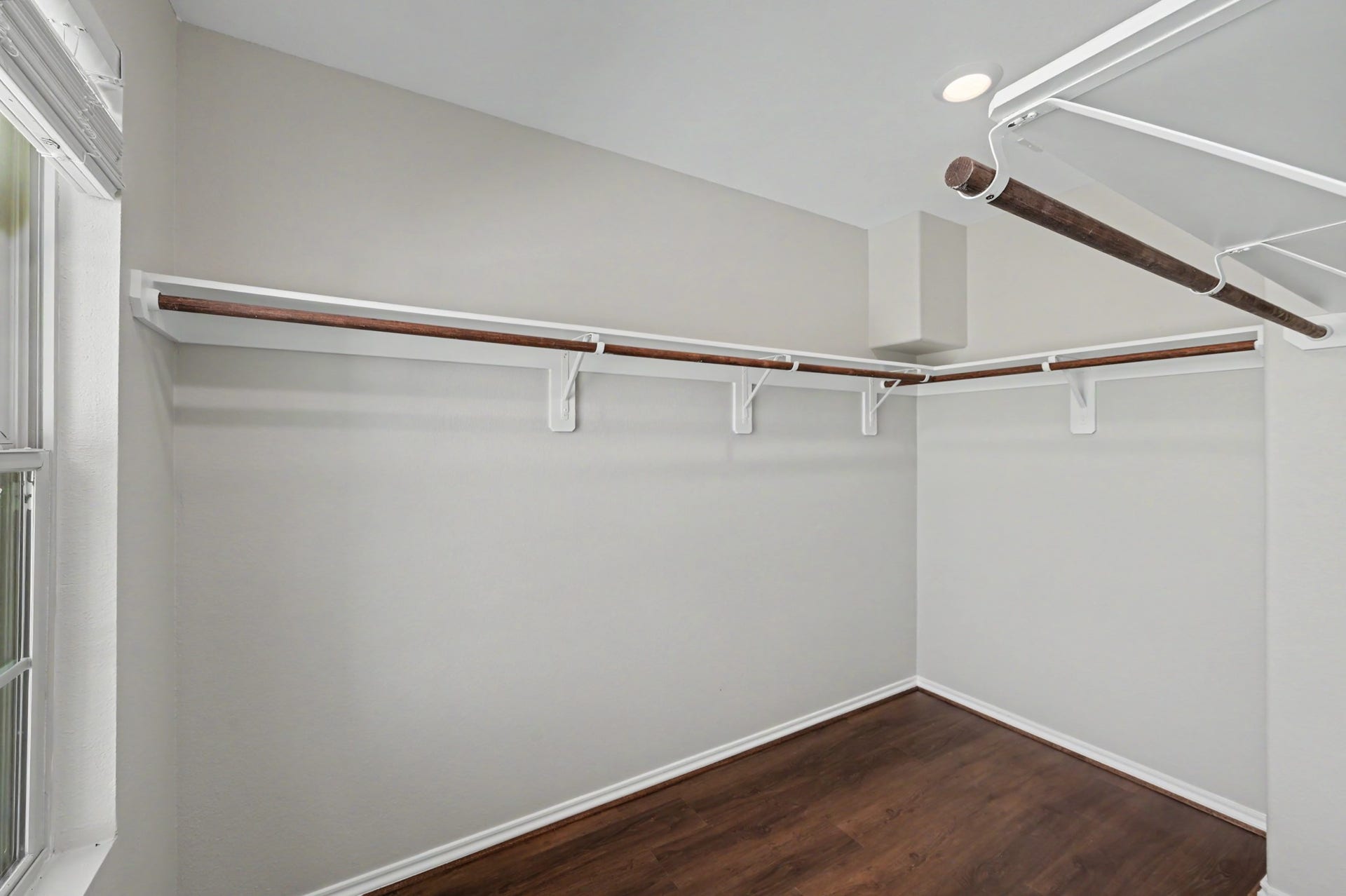 Spacious primary walk-in closet featuring wraparound shelving, hanging rods, wood-look flooring, and a window for natural light.
