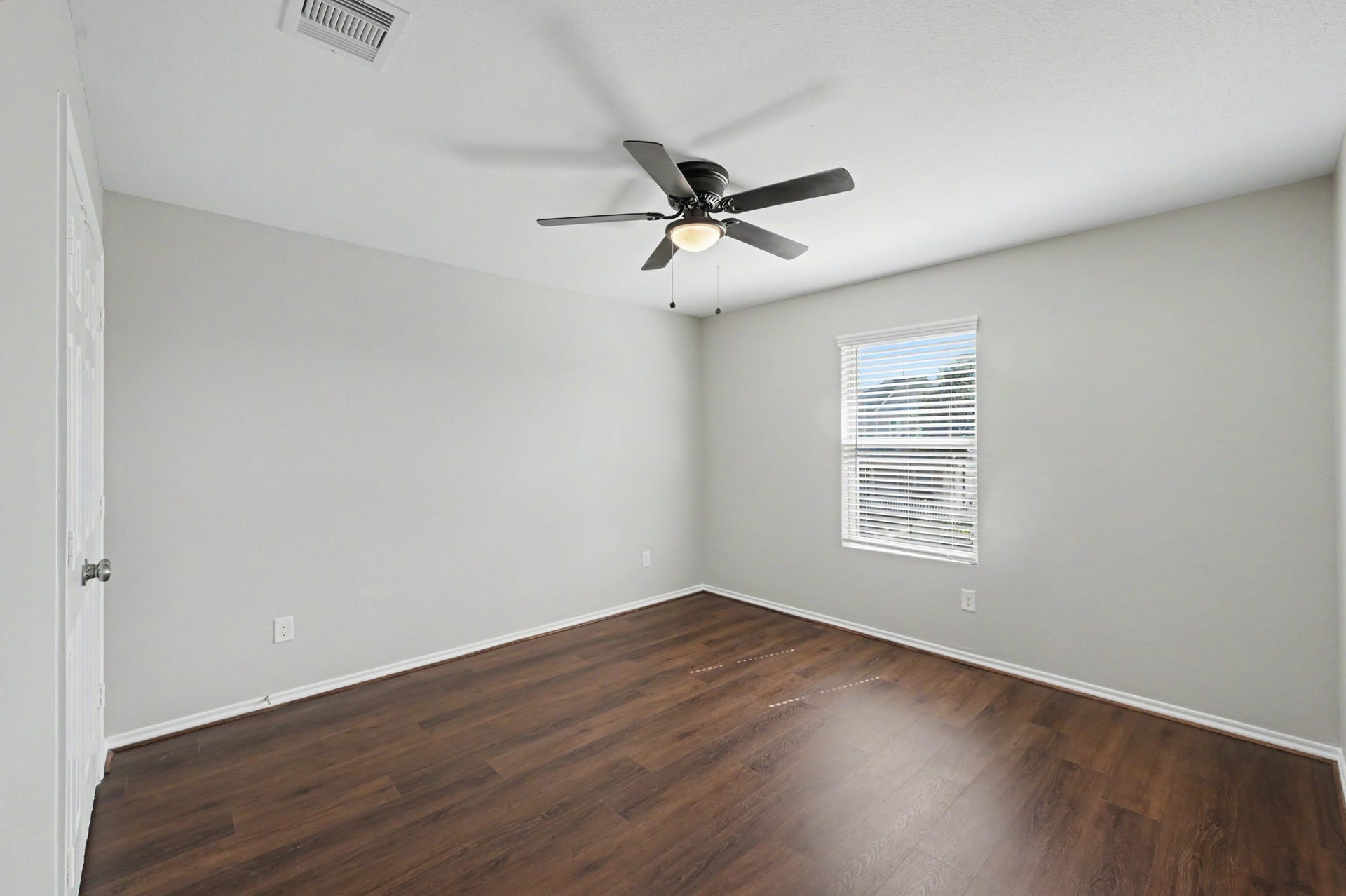 Spacious secondary bedroom featuring wood-look flooring, neutral paint tones, ceiling fan, and a large window providing natural light.